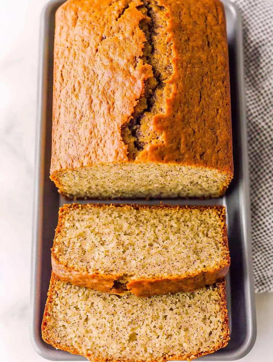 A hot banana loaf with cracked top and several pieces cut off sits displayed on a gray serving plate.