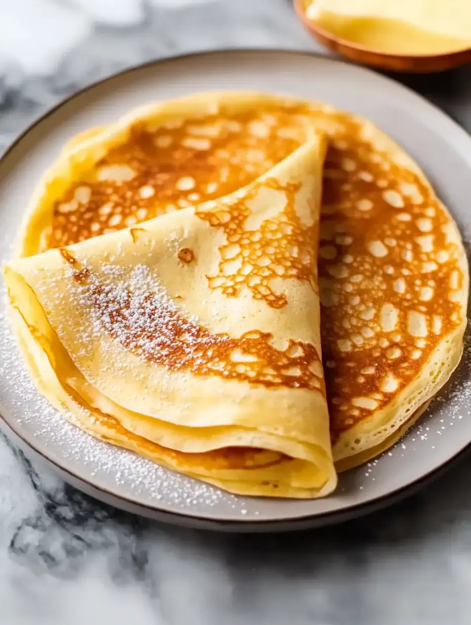 A serving of golden-brown thin pancakes lightly sprinkled with powdered sugar.