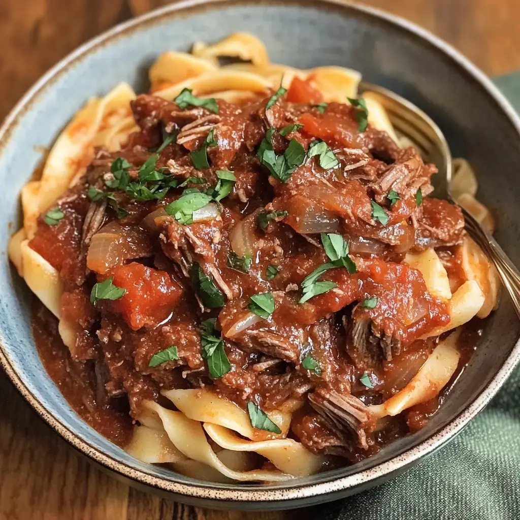 A comfy bowl of noodles dressed with chunky beef and tomato sauce, finished with green herbs.